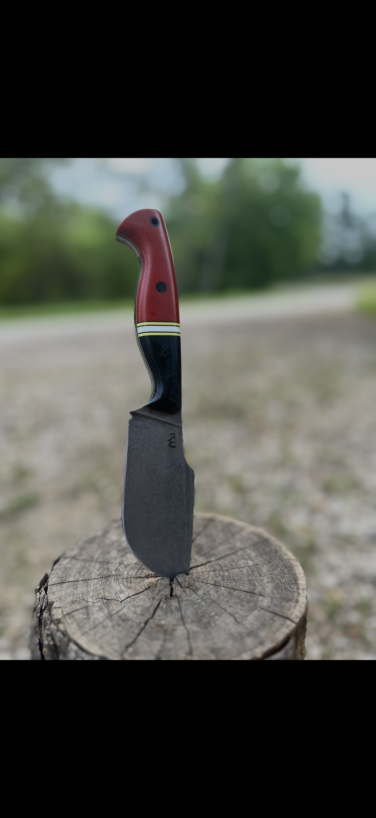 Knife with red G10 handle stuck in tree stump