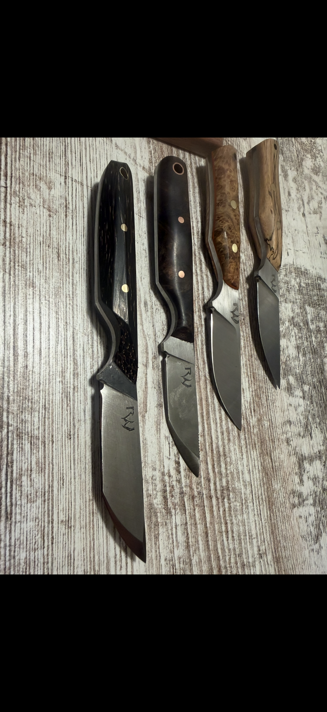 Four handcrafted knives with varied handles on wood surface